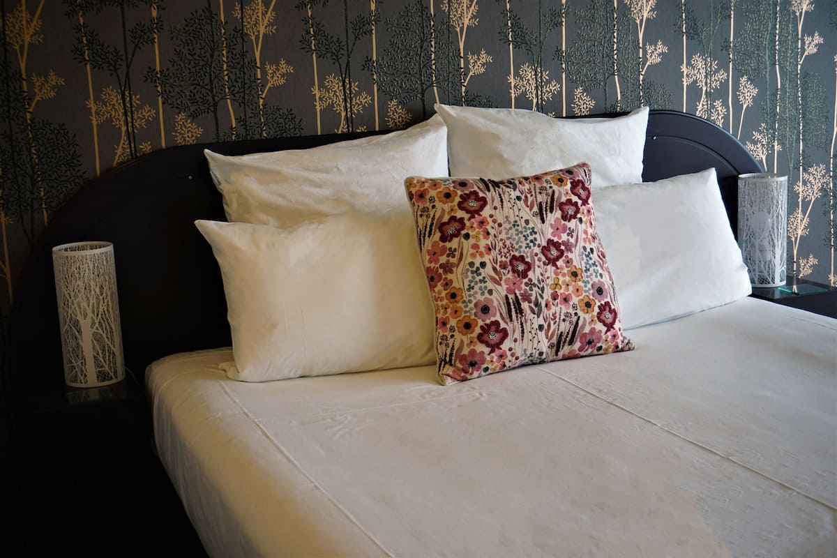 A bed with white and floral pillows, a dark headboard, and a wall with vertical patterns.