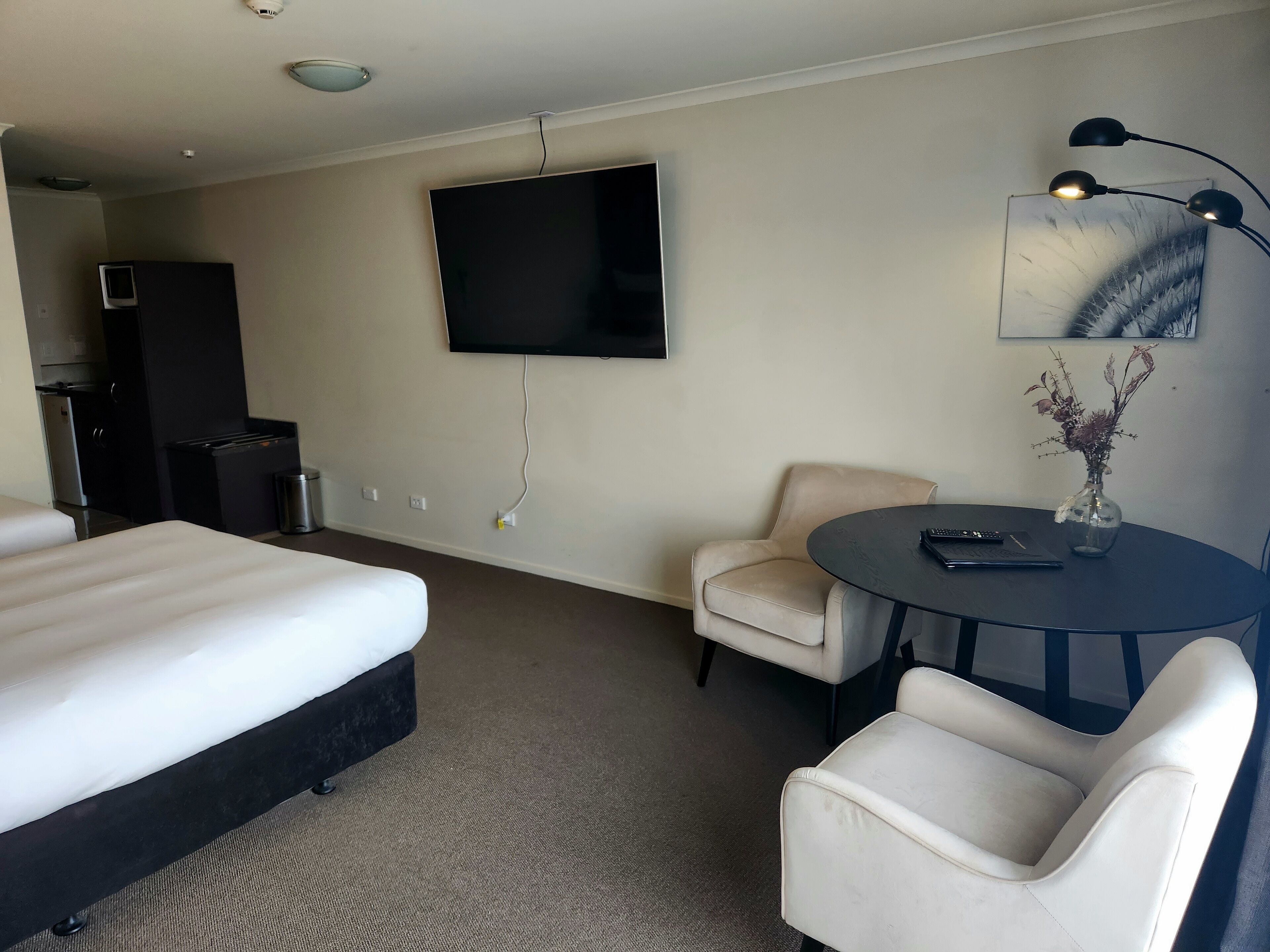 A hotel room with a bed, a desk, a chair, a TV, and a lamp.