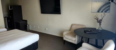 A hotel room with a bed, a desk, a chair, a TV, and a lamp.