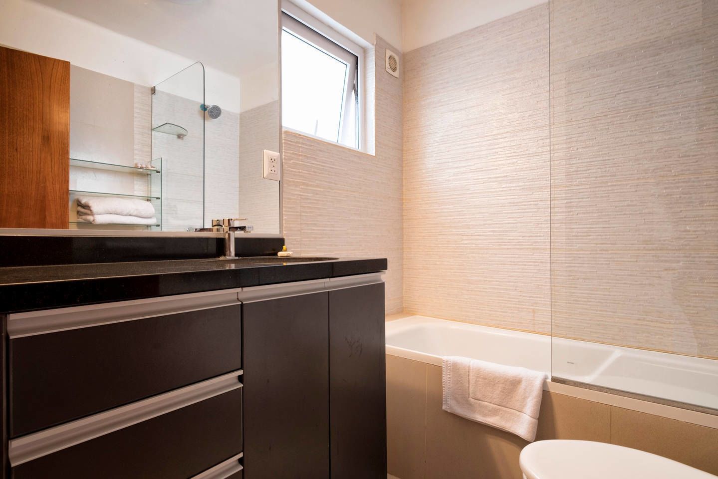 A modern bathroom with a dark wooden vanity, a glass shower enclosure, and a white bathtub.