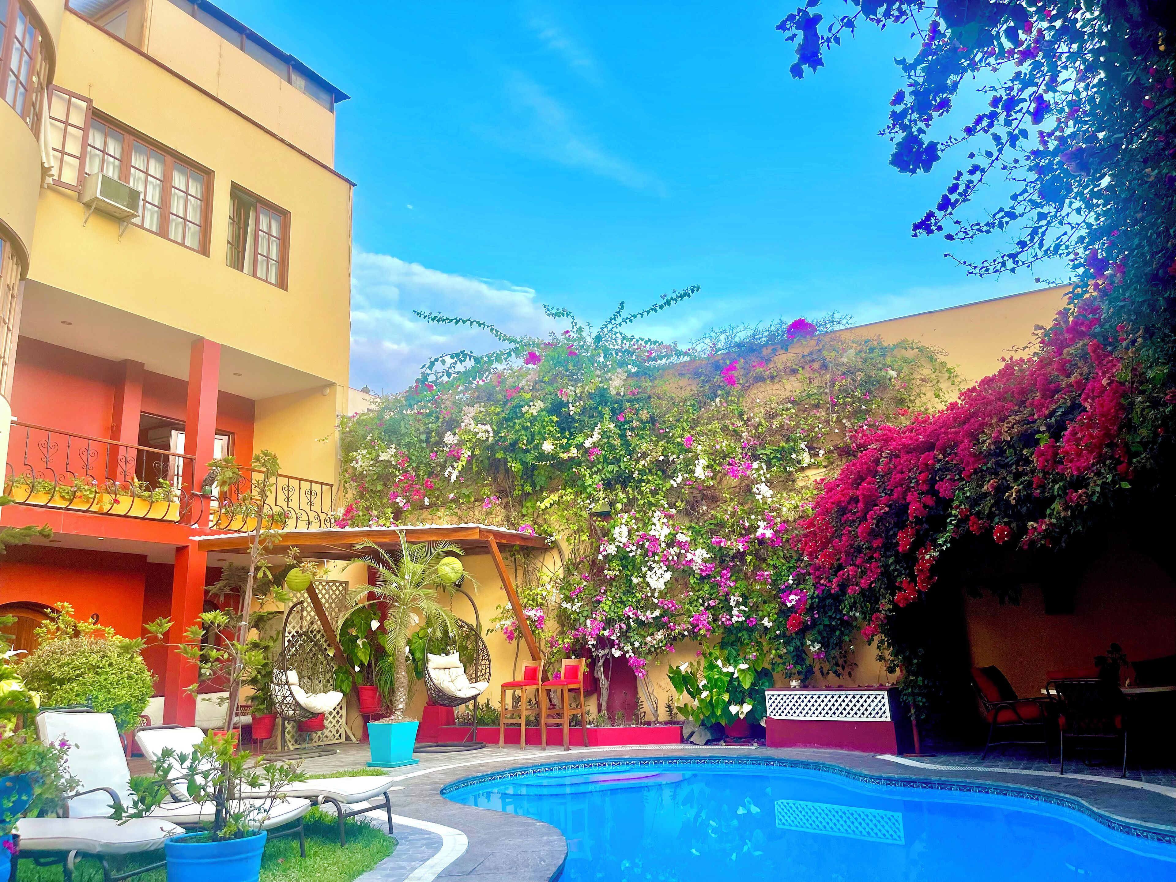 A pool area with lounge chairs, a pergola, and a building with balconies.