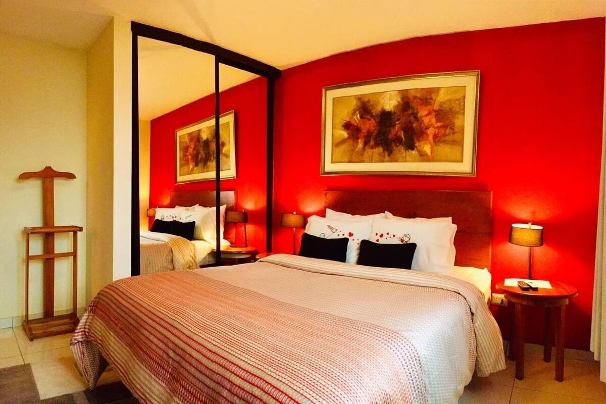 Habitación de hotel con una cama grande, un espejo y dos cuadros en la pared.