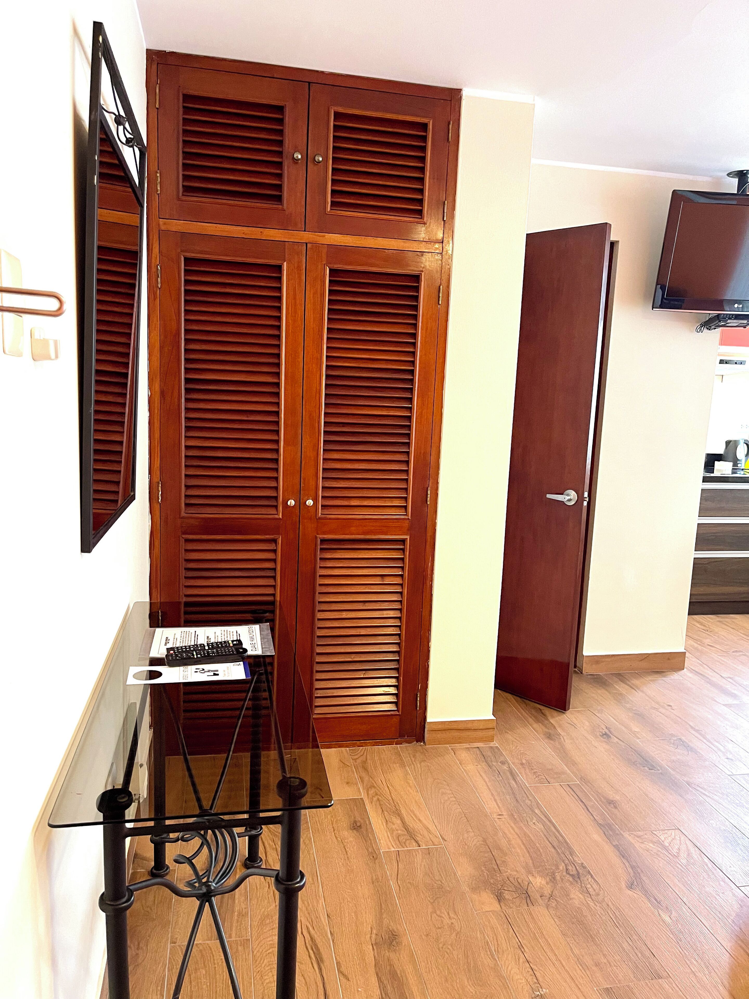 A room with a wooden wardrobe, a glass table with a keyboard, and a television on the wall.