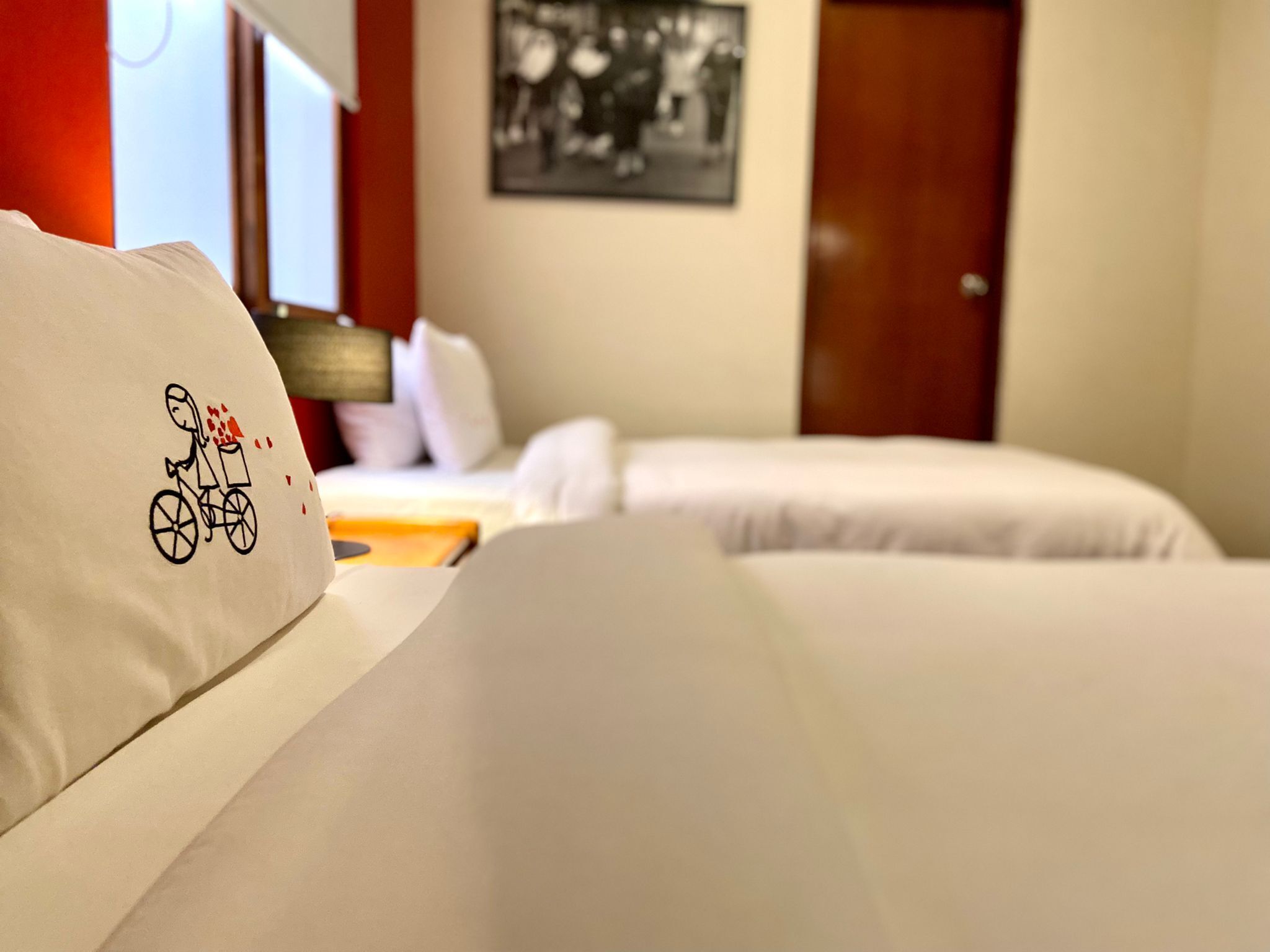 A hotel room with two beds, a window with a view, a door, and a wall with a framed picture.
