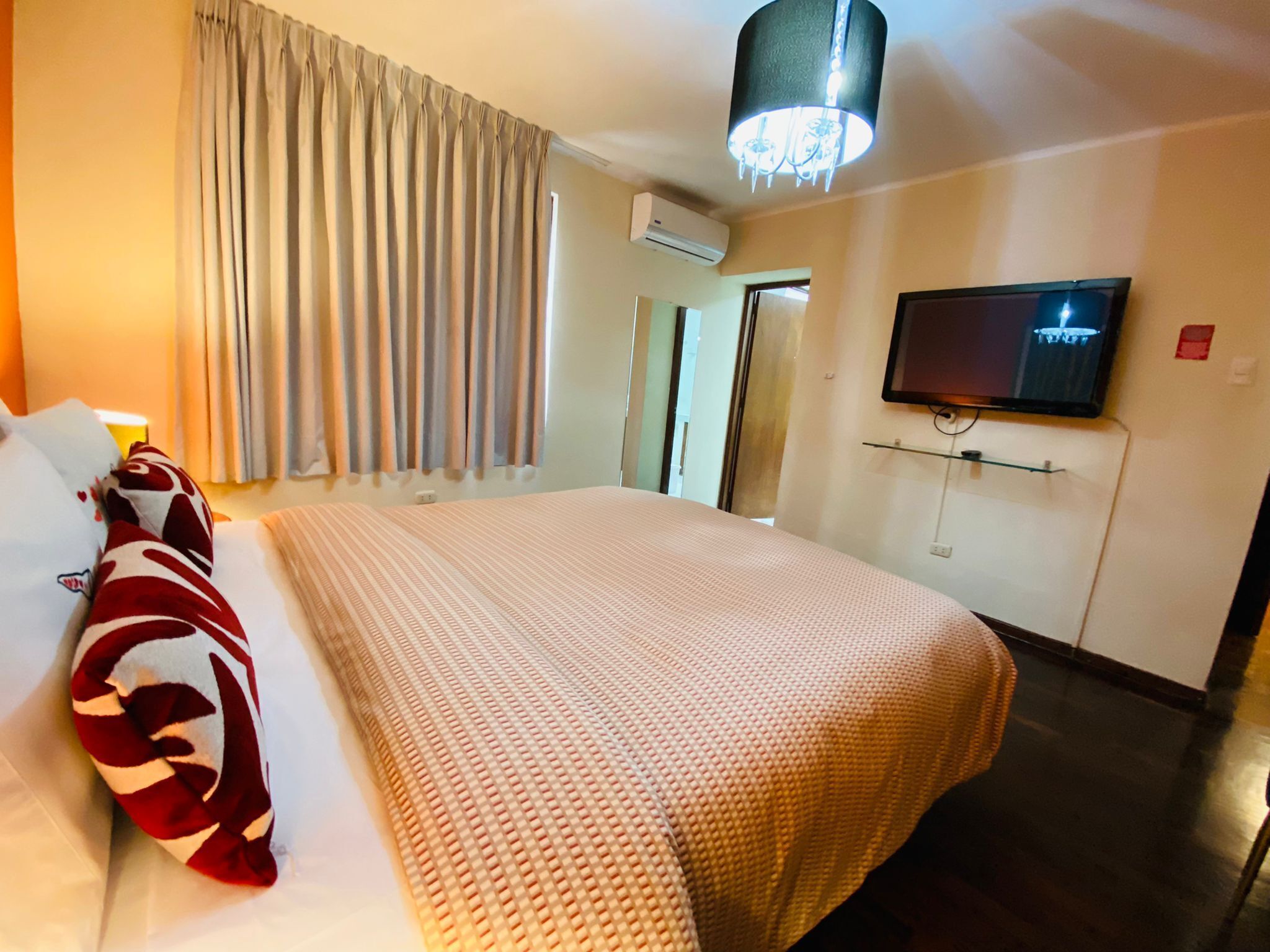 Habitación de hotel con una cama grande, televisor en la pared, aire acondicionado y un candelabro.
