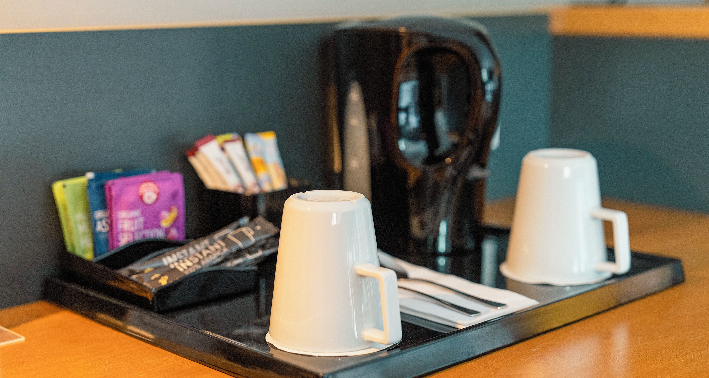 Eine Kaffeestation mit zwei weißen Tassen, einer Kaffeemaschine und einer Ablage für Kaffeekapseln.