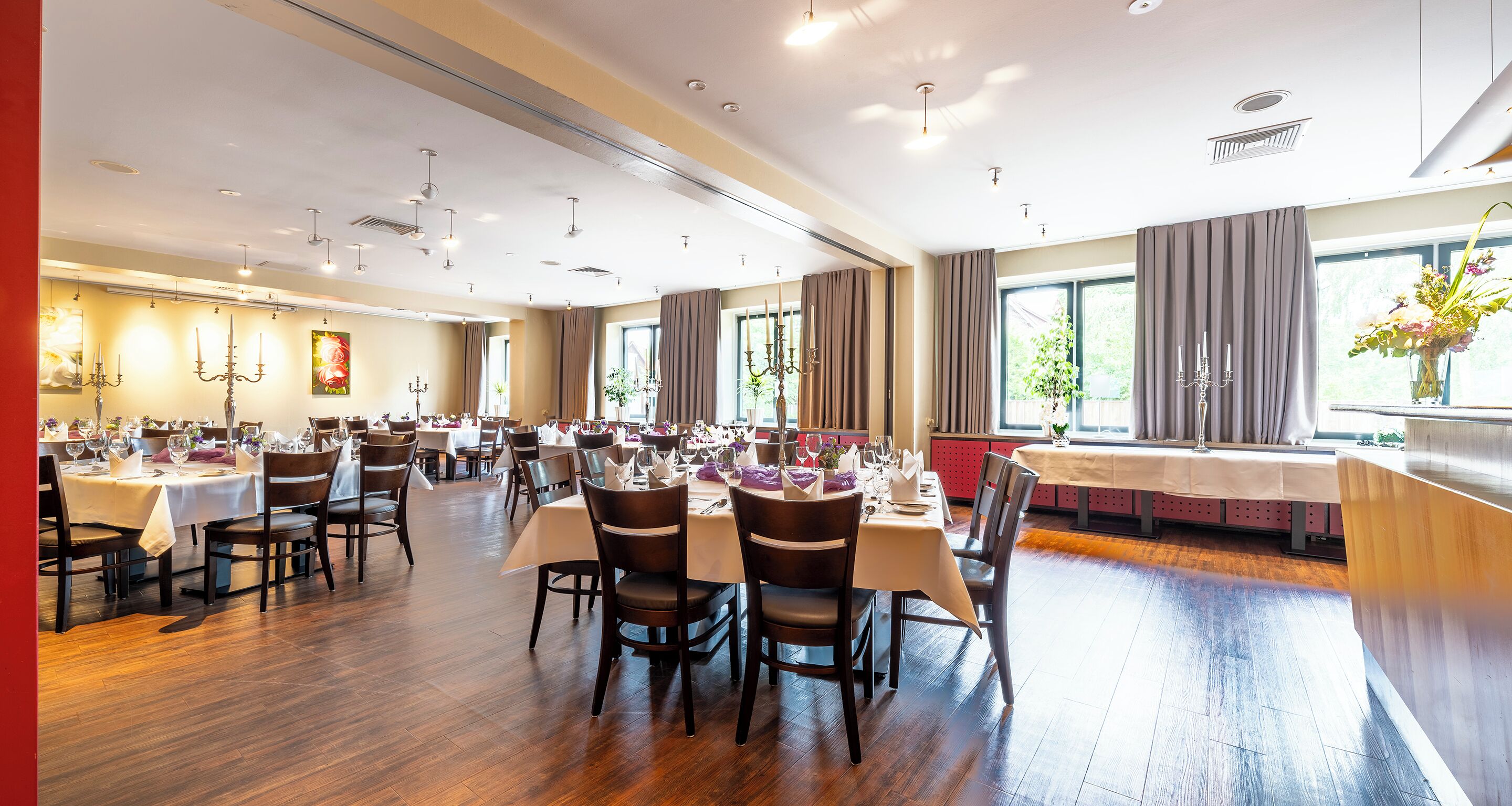 A spacious dining area with multiple tables and chairs, large windows, and modern lighting fixtures.