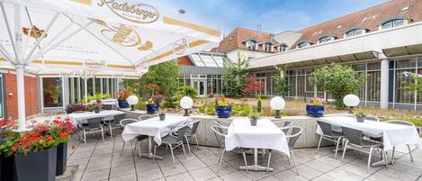 An outdoor patio area with tables and chairs, a large umbrella, and potted plants.