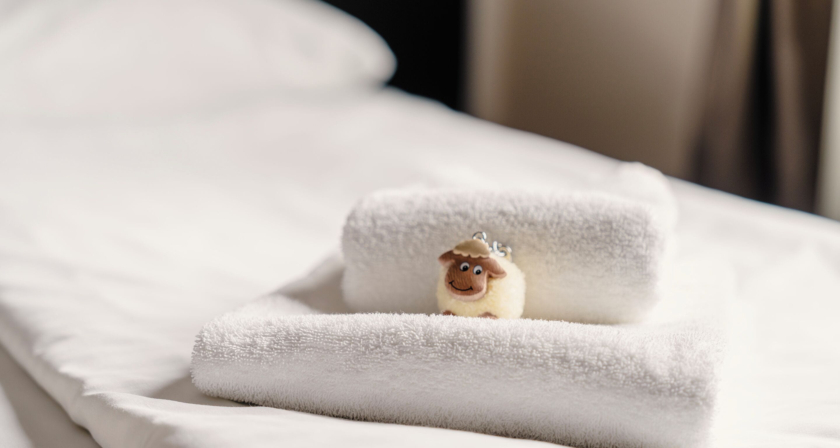 A neatly folded white towel on a bed with a plush toy in the center.