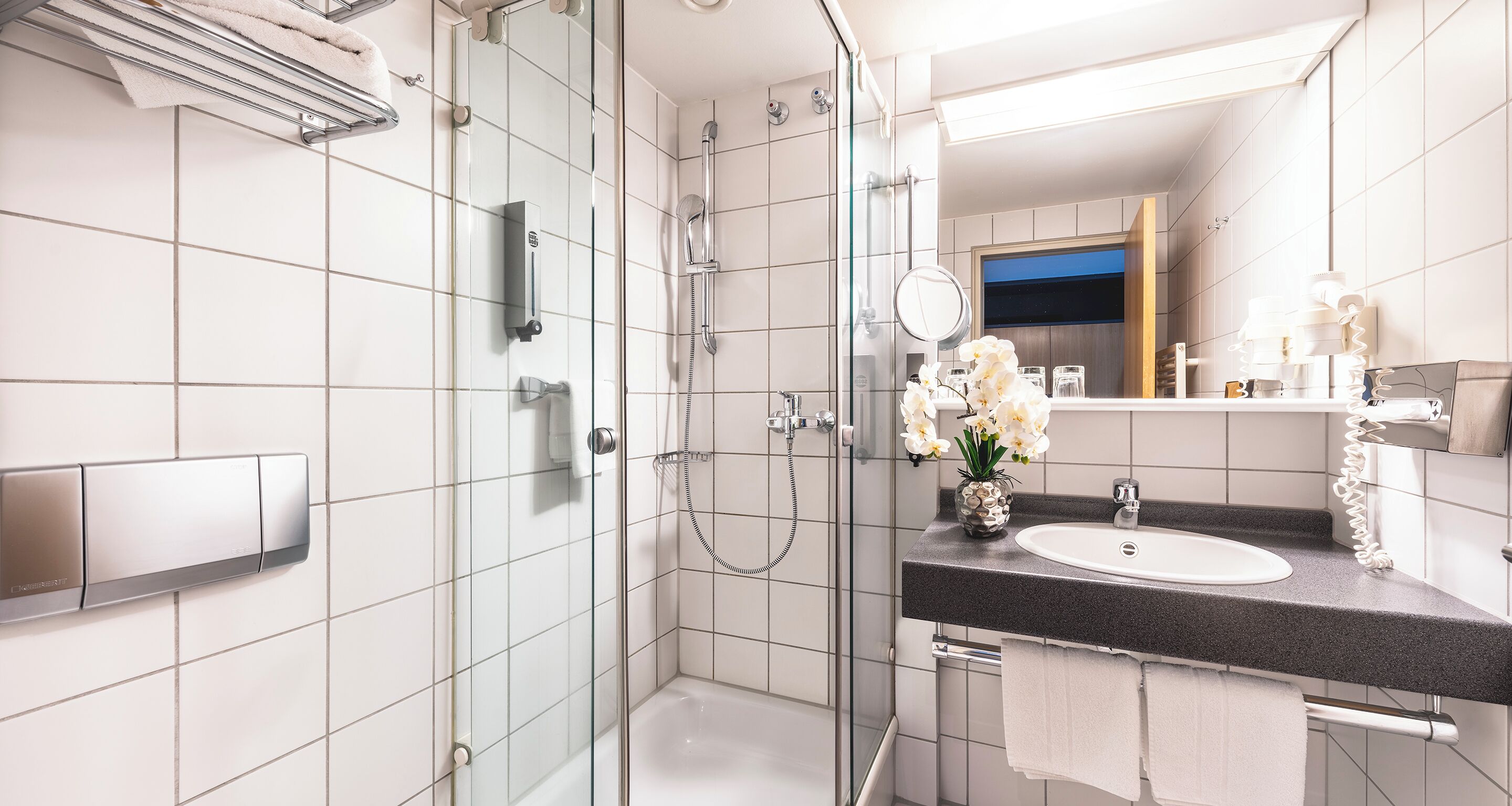 Un baño moderno con ducha envuelta en vidrio, lavamanos blanco y tocador con espejo.