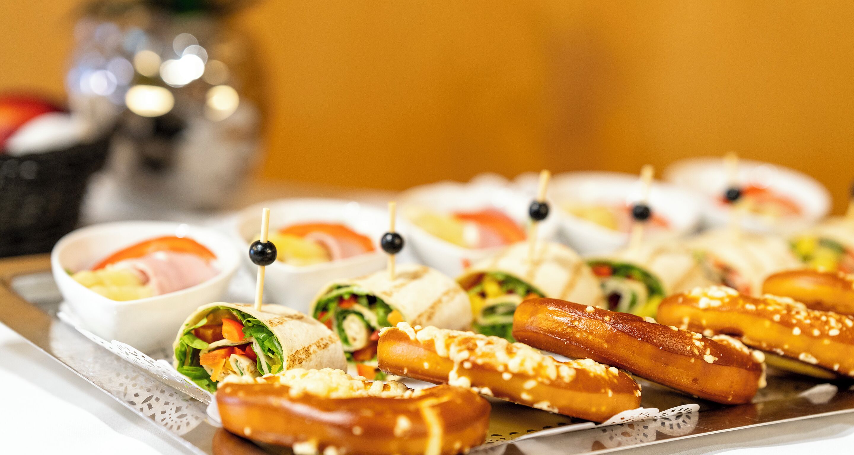 A tray of food items including wraps, sausages, and small bowls of dipping sauces.