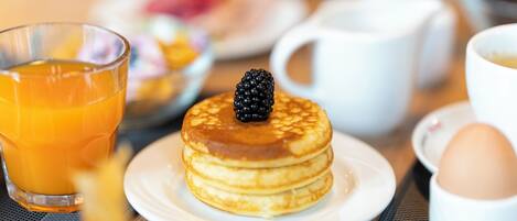 Desayuno con tortitas, un vaso de jugo de naranja y una taza de café.