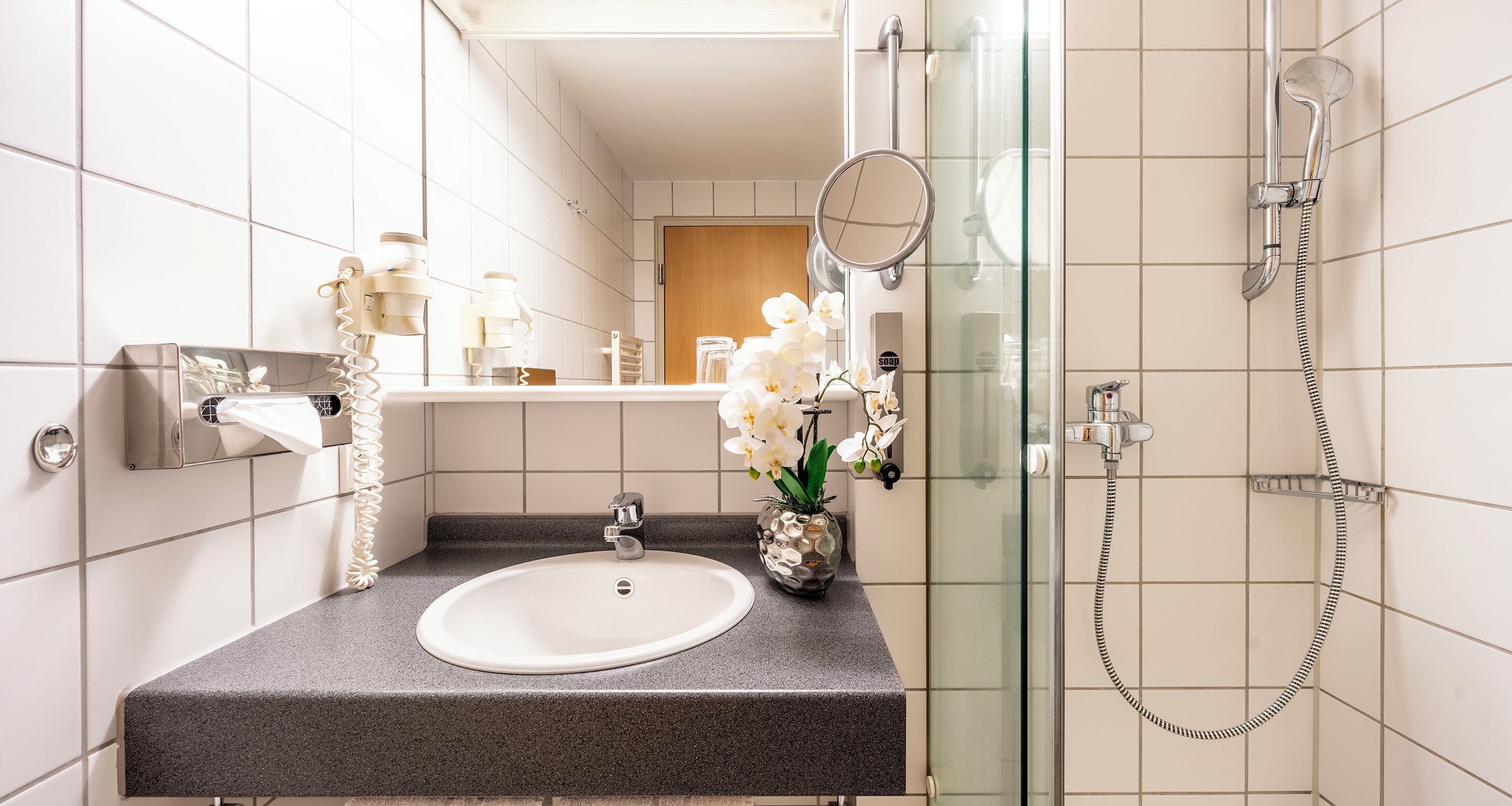 A bathroom with a white sink, a mirror, a glass shower enclosure, and a towel rack.