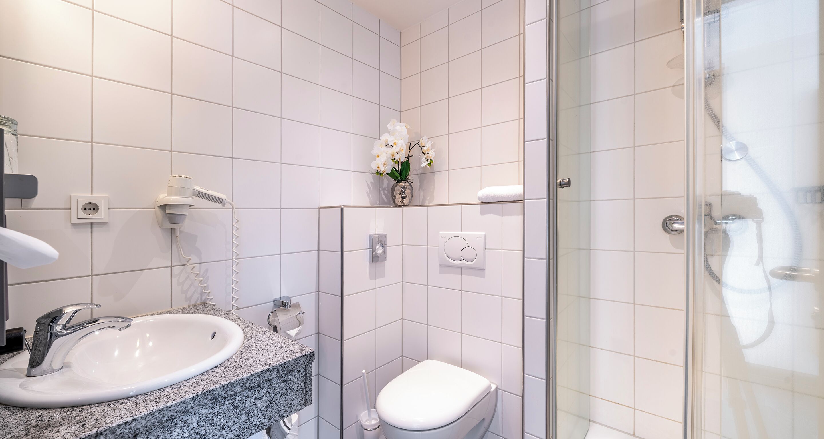 A modern bathroom with a granite countertop sink, a toilet, and a glass-enclosed shower.