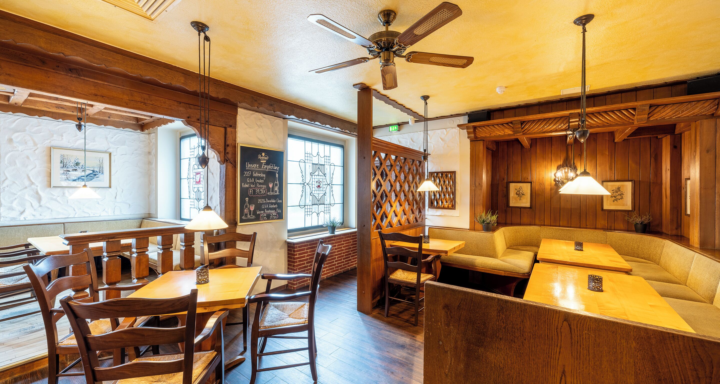 L’intérieur d’un restaurant est aménagé avec des meubles en bois, un ventilateur de plafond et un menu écrit à la craie sur un tableau noir.