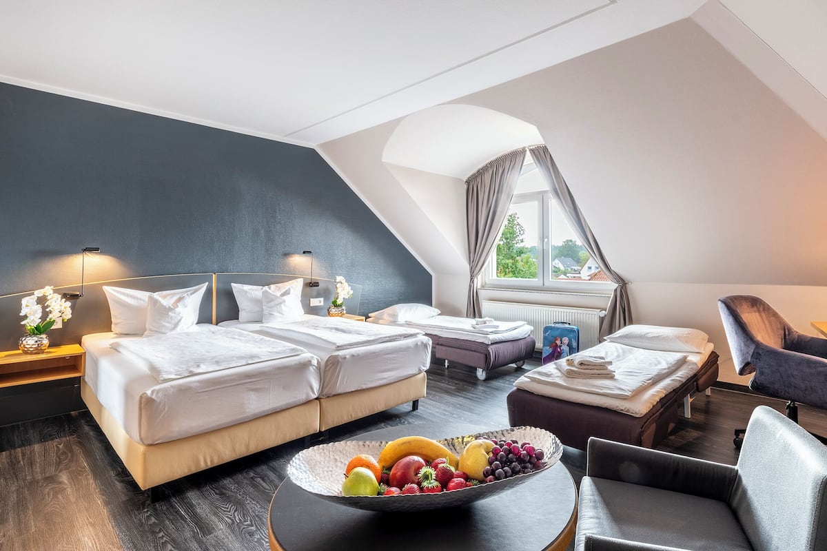 A modern hotel room with two beds, a desk, and a dining area.