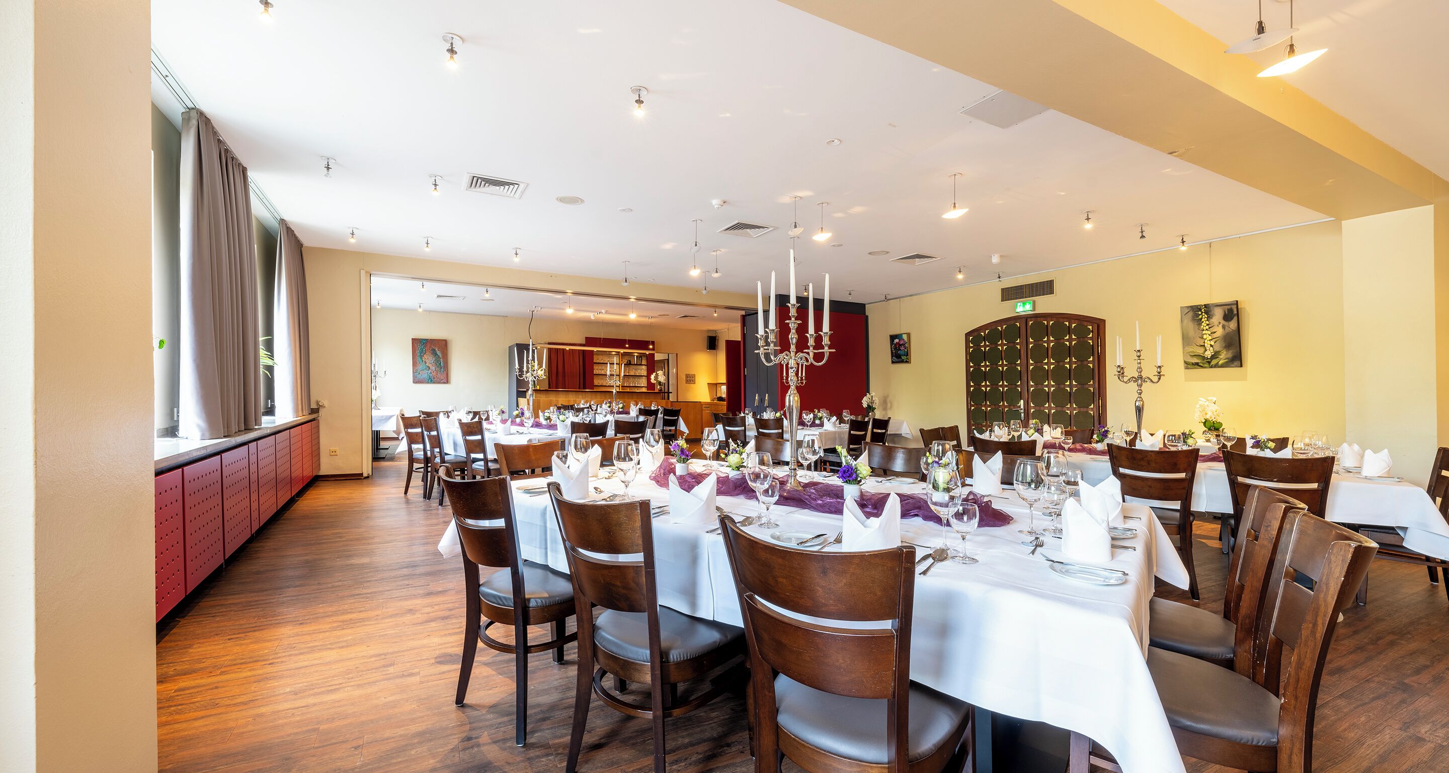 Un restaurant avec de nombreuses tables dressées pour le service, un plancher en bois et un lustre.