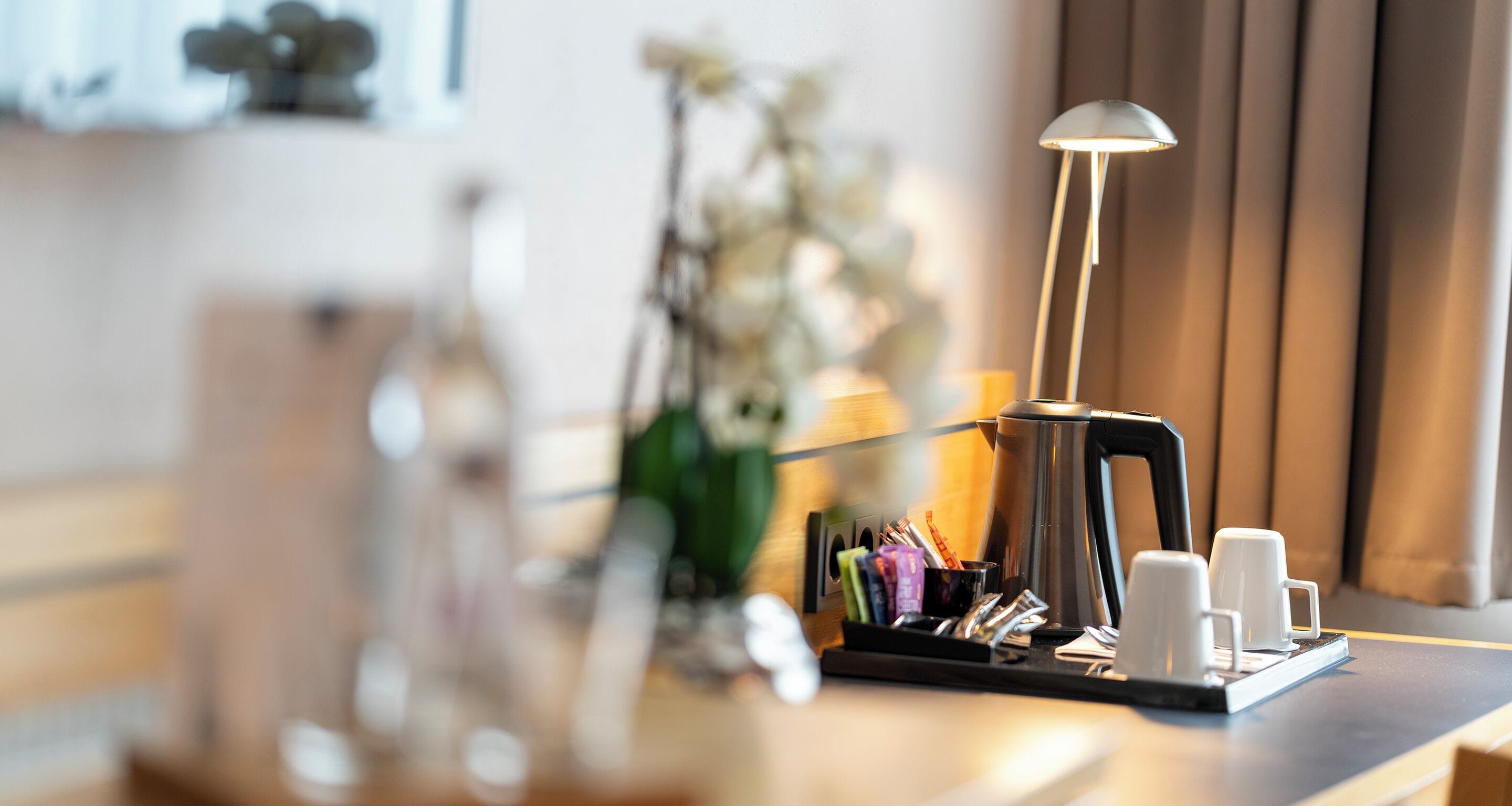 A coffee station with a kettle, cups, and a tray of utensils.