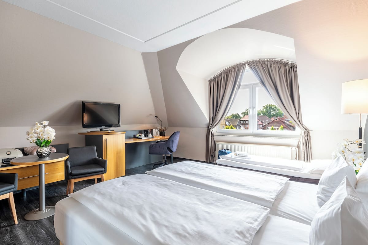 A hotel room with a bed, a desk, a chair, a television, and a window with curtains.