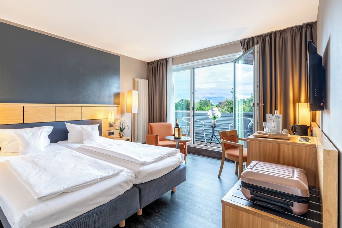 A hotel room with two beds, a desk, a chair, a TV, and a view of the outdoors.