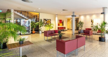 Un vestíbulo amplio con asientos rojos, plantas en macetas y una escalera.