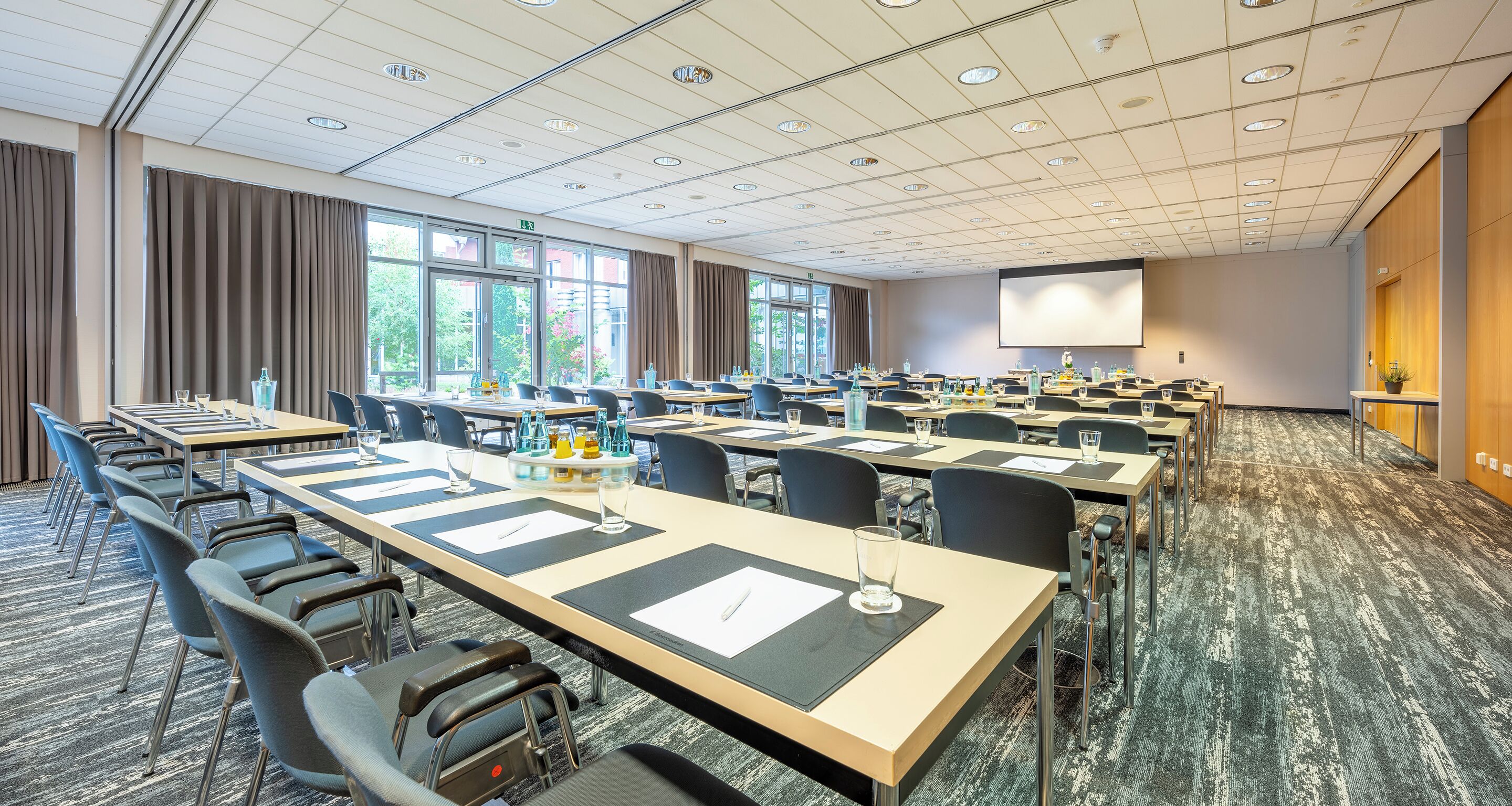 A conference room with multiple tables, chairs, and a large screen.