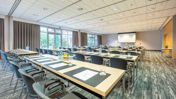 A conference room with multiple tables, chairs, and a large screen.