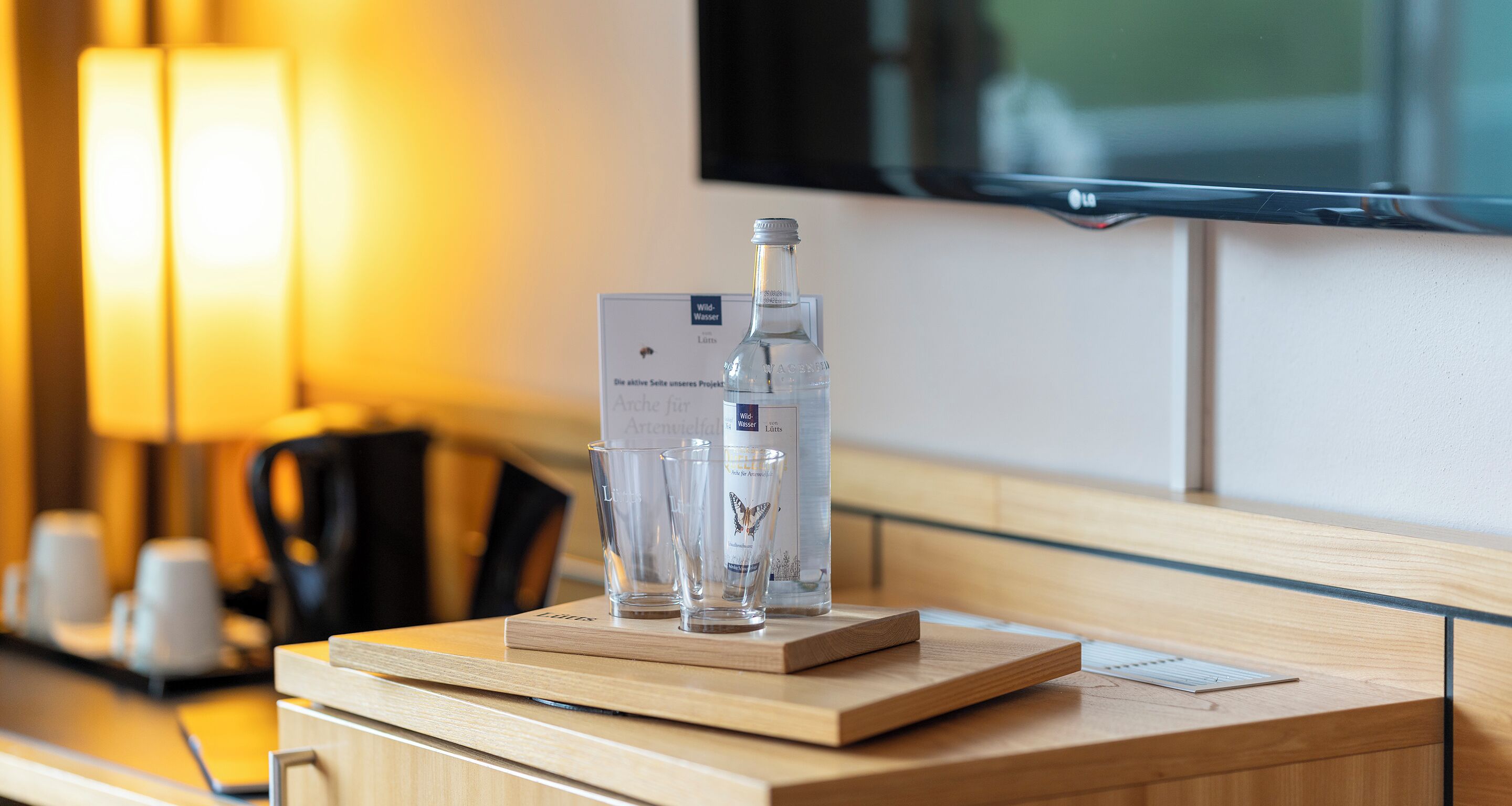 Une chambre d’hôtel avec un bureau en bois, une bouteille d’eau et deux verres sur un plateau.