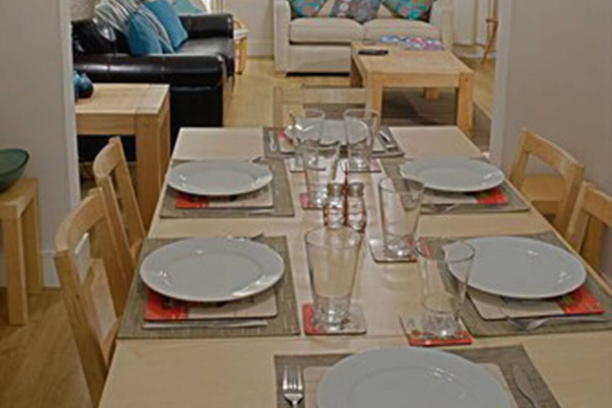 A dining area with a table set for four, chairs, and a sofa in the background.