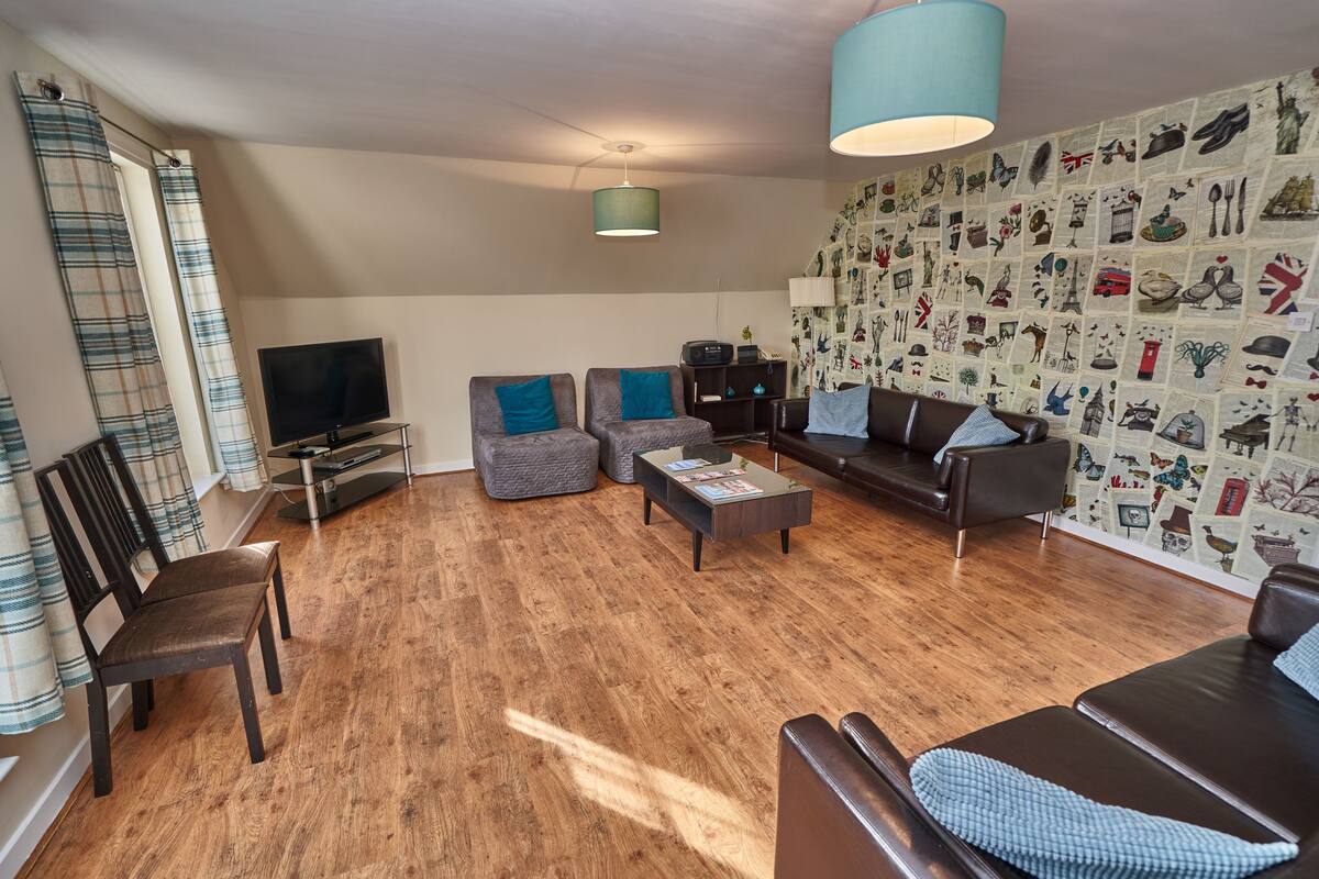 A living room with a television, two sofas, a coffee table, and a wall decorated with illustrations.