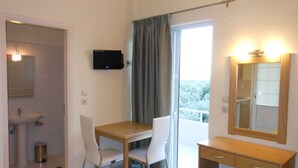 Ein Zimmer mit Holztisch, zwei weißen Stühlen, einer kleinen Holzkabine, einem Spiegel und einem an der Wand befestigten Fernseher.
