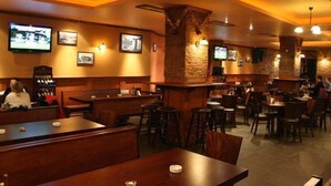 A restaurant interior with wooden tables and chairs, stone pillars, and wall-mounted televisions. - Elegant Lodge Hotel (Bansko)