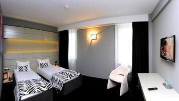 Una camera d'albergo con due letti, una scrivania, una sedia, una televisione e una lampada a parete.