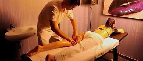A massage therapy session in a room with a sink and a painting of lips on the wall.