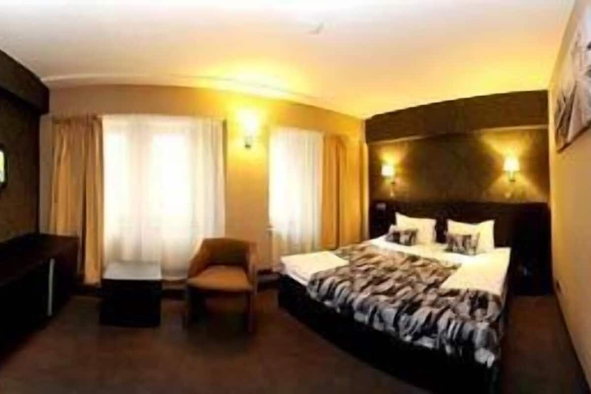 A hotel room with a bed, a desk, a chair, and a large mirror.