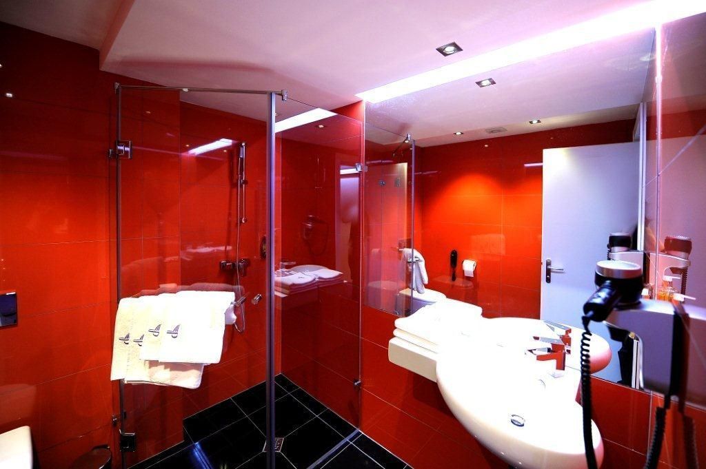 A modern bathroom with red tiles, a glass shower enclosure, a white sink, and a mirror.