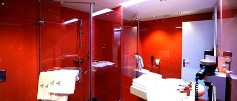A modern bathroom with red tiles, a glass shower enclosure, a white sink, and a mirror.