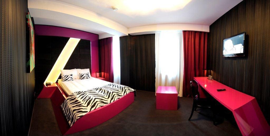A modern hotel room with a curved bed, a desk, and a television on the wall.