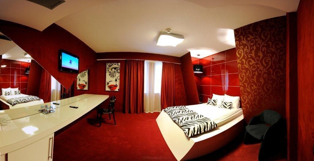 Una habitación de hotel con una cama curvada, un escritorio con una silla, un televisor y cortinas rojas.