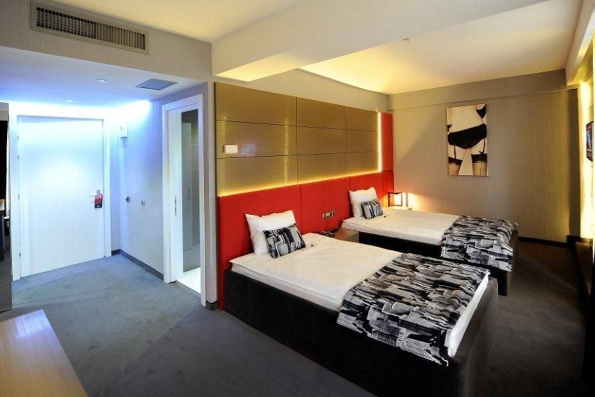 A hotel room with two beds, a red accent wall, a large mirror, and a modern design.