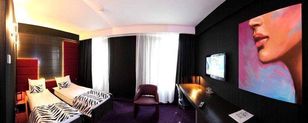 A hotel room with two beds, a desk, a chair, a TV, and a large painting on the wall.