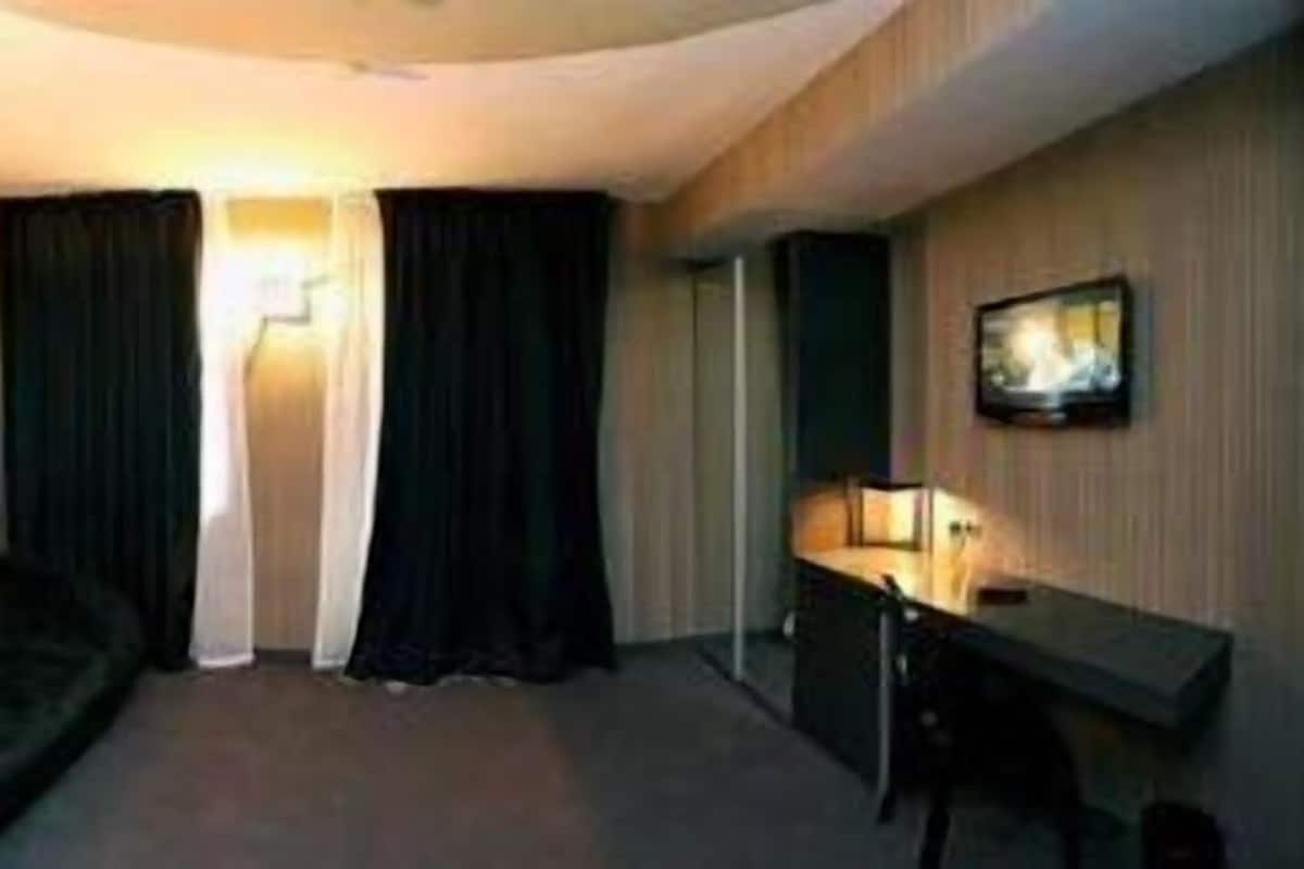 A hotel room with a dark-colored sofa, a desk with a lamp, and a television mounted on the wall.