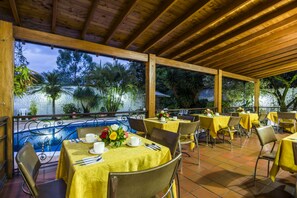 An outdoor dining area with yellow tablecloths, metal chairs, and a view of trees and a pool. - Hotel Portales Del Campestre (Medellín)