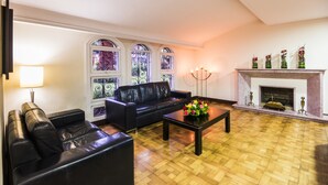 Uma sala de estar com um sofá de couro preto, uma mesa de centro com flores, uma lareira e janelas de vitral.