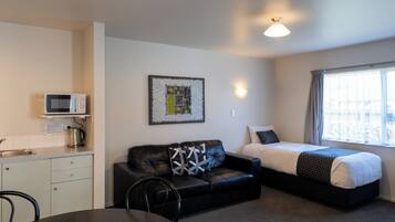 A compact room with a kitchenette, a black leather sofa, a bed, and a dining table.