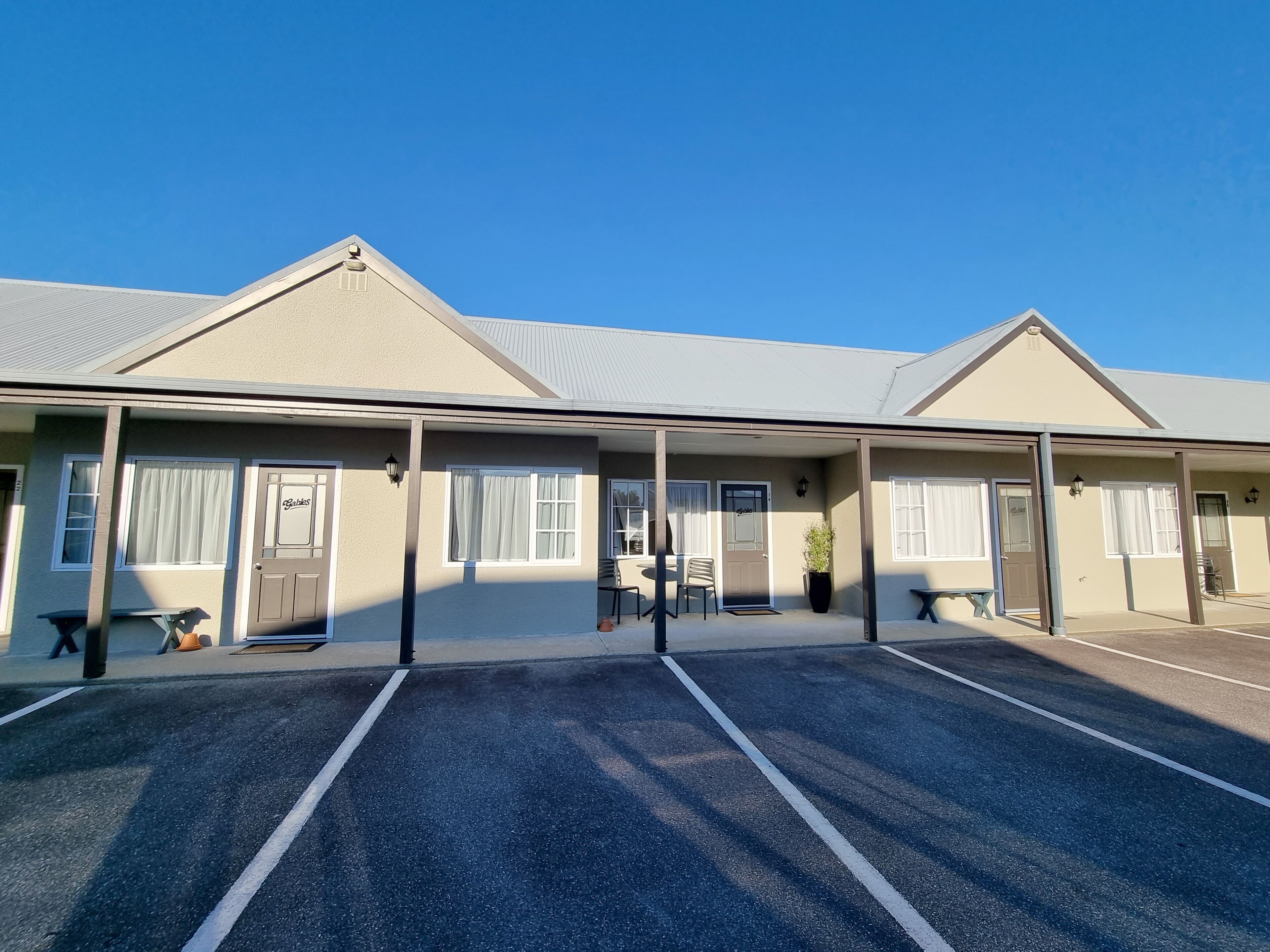 A motel with a covered parking area, multiple rooms with windows, and a small outdoor seating area.