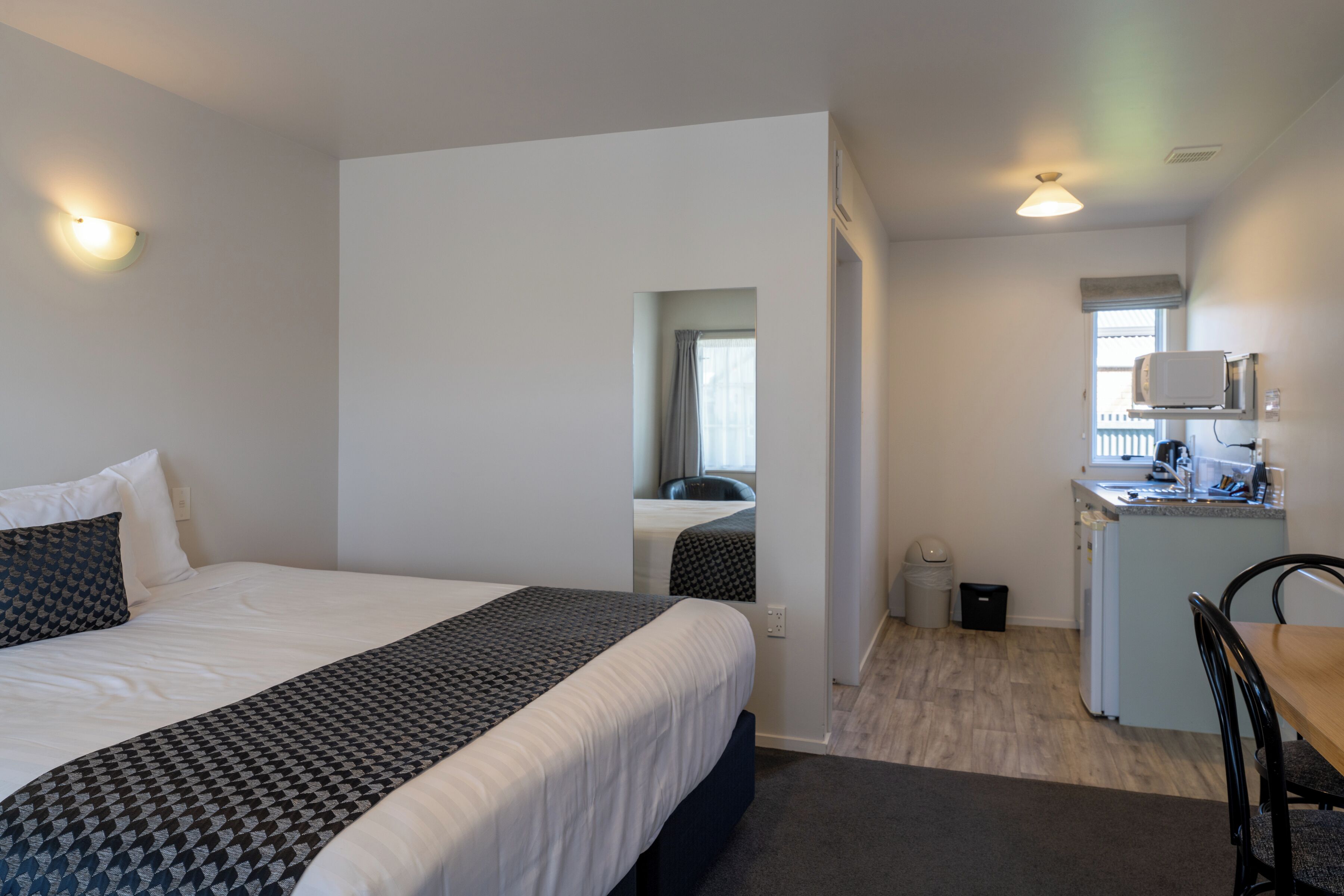 Quarto de hotel com cama, escrivaninha e cozinha compacta.