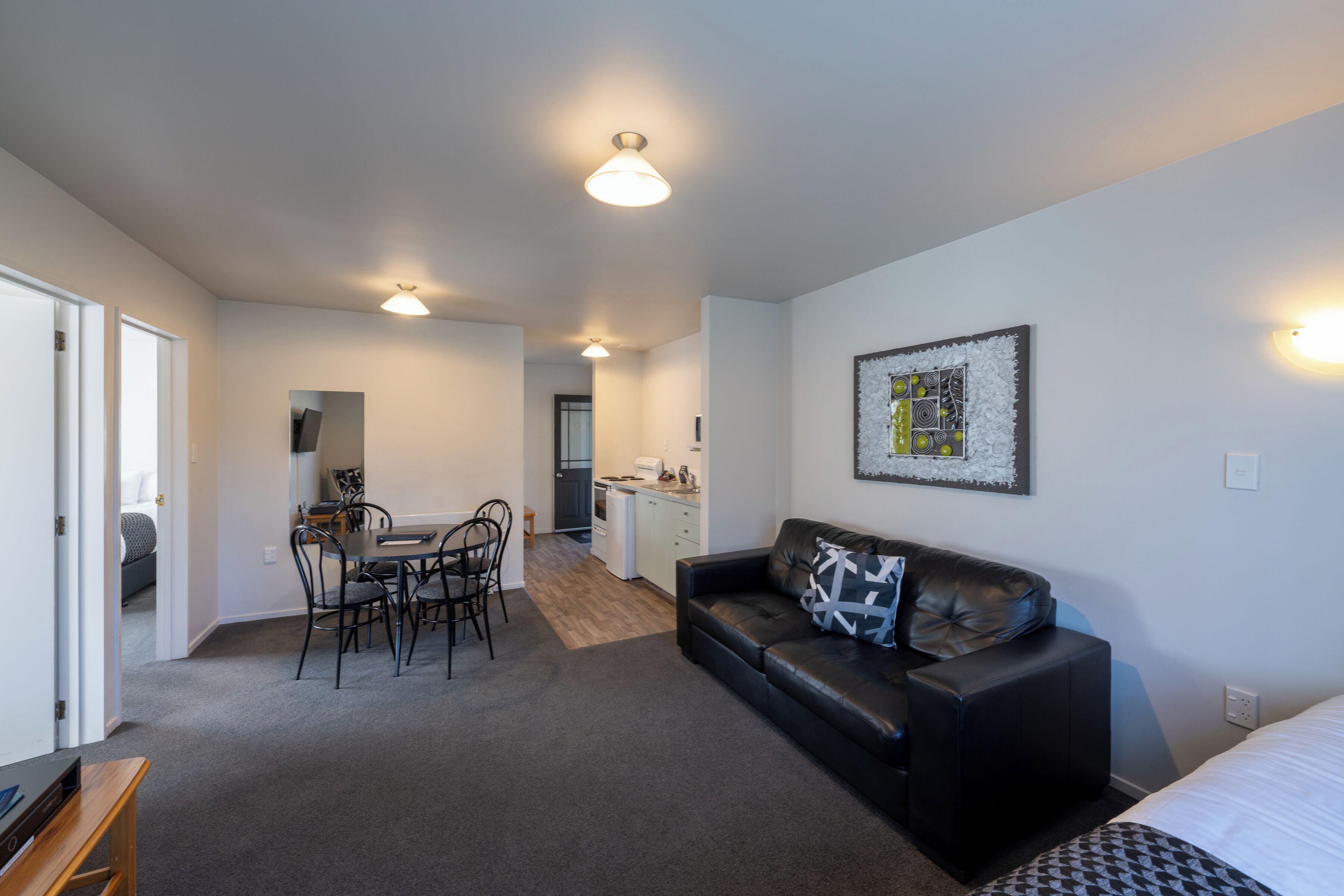 Un appartement moderne comprenant un coin repas, un salon avec un canapé en cuir noir et une cuisine à l’arrière-plan.