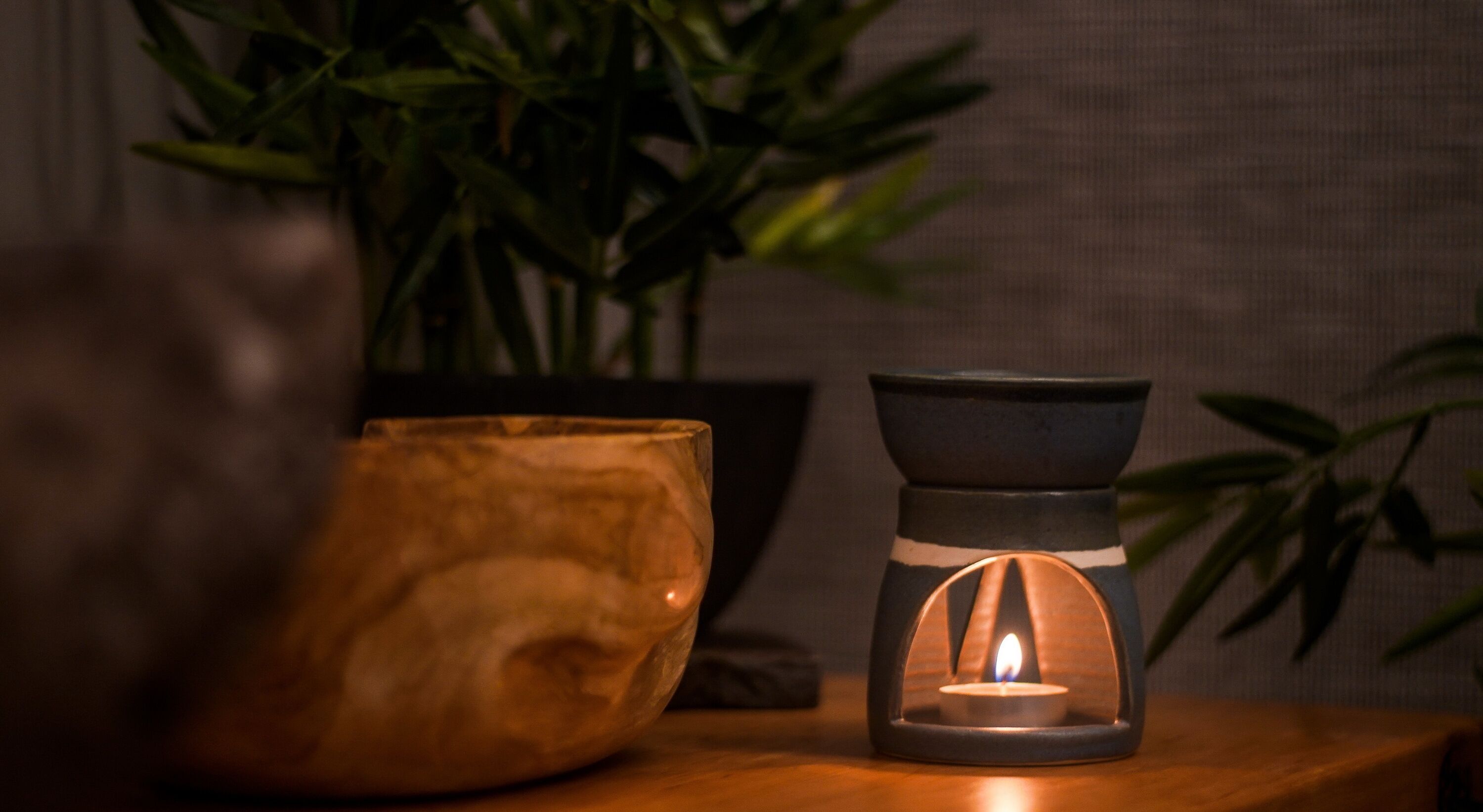 A wooden bowl and a candle holder with a lit candle on a wooden surface.