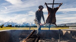 Una persona colgando un gran cadáver animal en una estructura de madera al aire libre, con montañas al fondo.